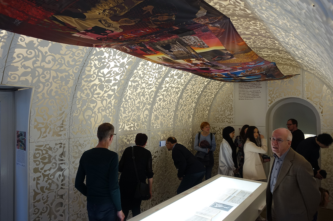 eine Gruppe von Menschen geht durch einen Ausstellungsraum und schaut sich alles interessiert an