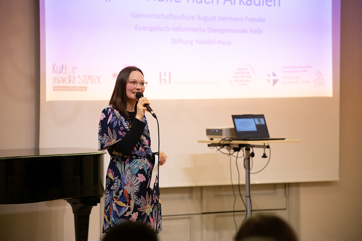 Eine Frau steht vor einer Leinwand und spricht in ein Mikro