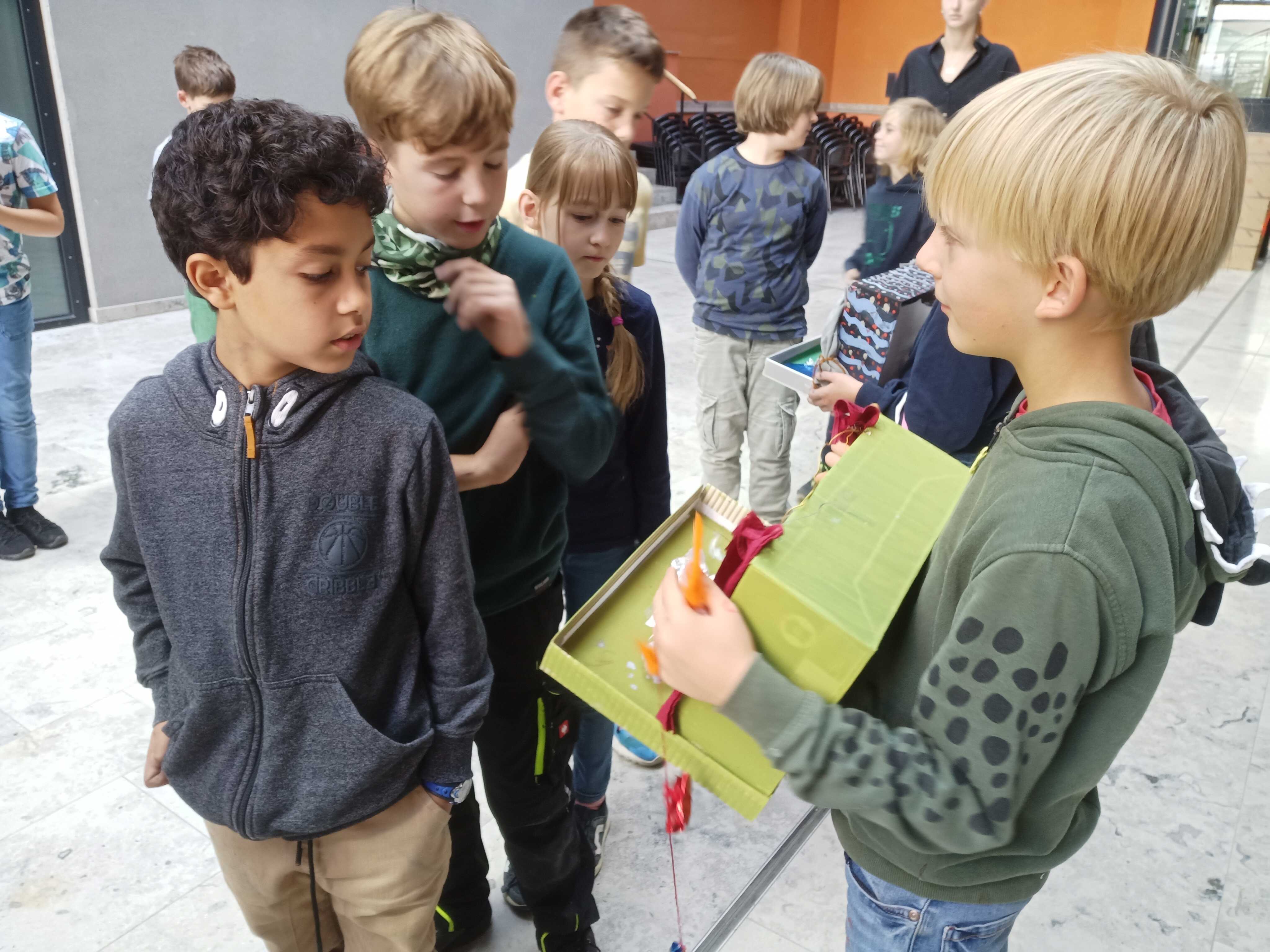 ein blonder Junge zeigt sein Bühnenbild im Schuhkarton einer Gruppe anderer Kinder