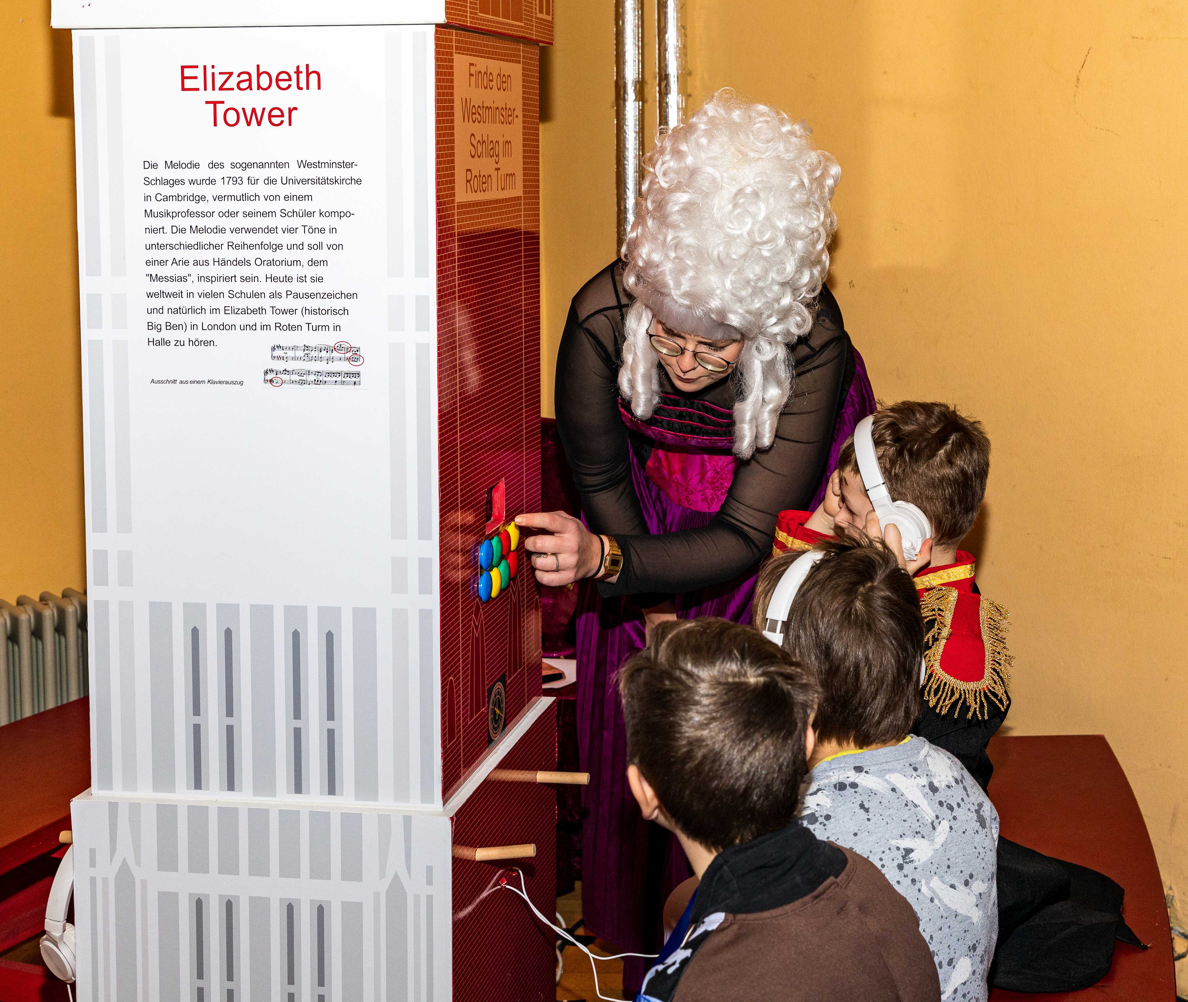 eine Person mit einer weißen Lockenperücke erklärt Kindern ein Ausstellungsstück 