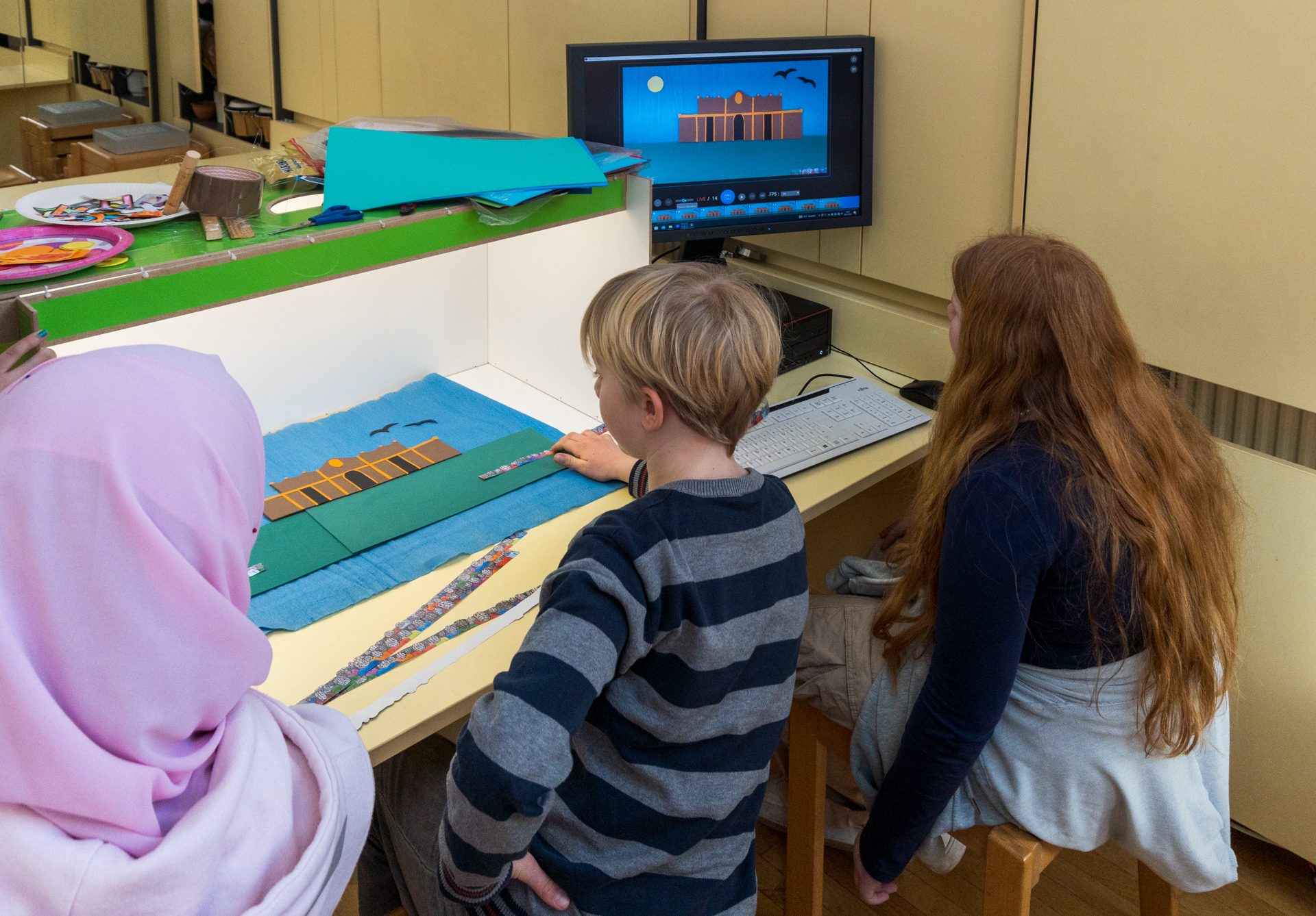 Rückenansicht von drei Kindern, die an einem Tisch sitzen und einen Stop-Motion-Film erstellen