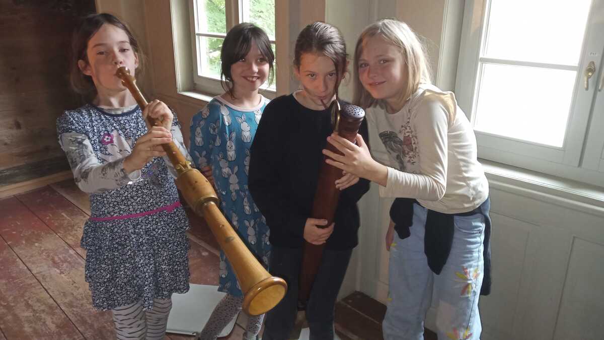 eine Gruppe von 4 Mädchen steht vor einem Fenster, das Mädchen ganz links spielt ein Blasinstrument